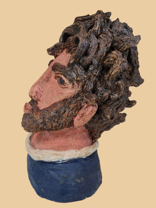 Ceramic bust of a man with textured hair and blue garment on a white background