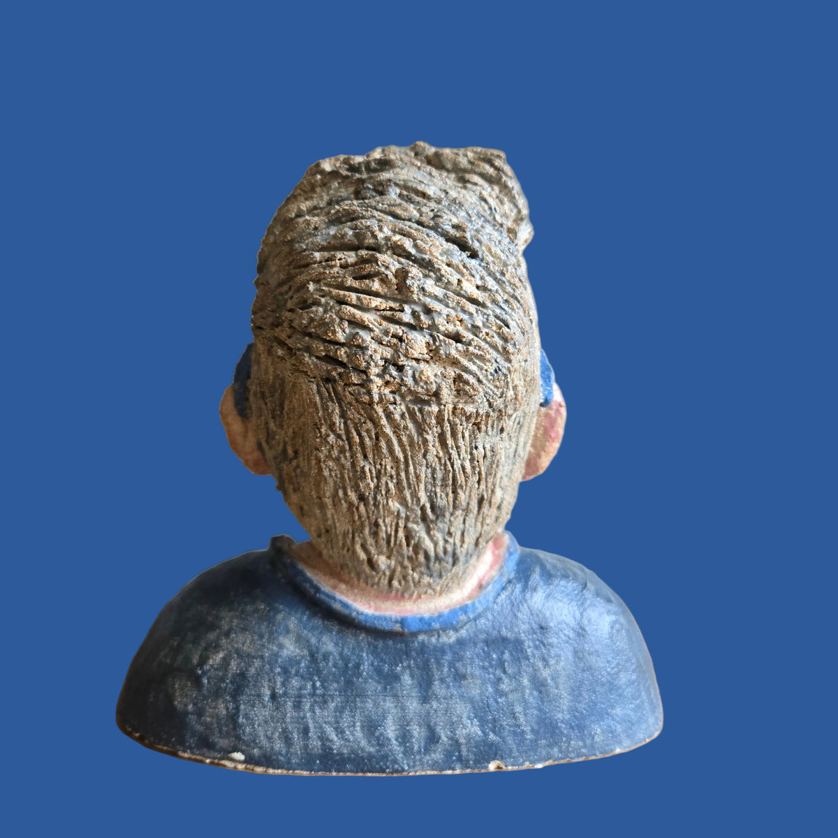 A textured sculptural bust of a person viewed from the back, featuring a matted brown hair texture and a blue shirt.